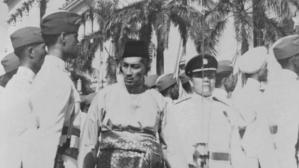 Yusof Ishak, mengenakan peci, sedang meninjau barisan pada Hari Kebangsaan (sumber : beritaharian.sg) 